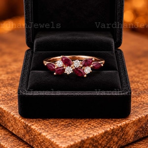 May include: A rose gold ring featuring a cluster of marquise-cut deep red rubies and round brilliant-cut white diamonds arranged in a floral-inspired pattern, presented inside a black velvet jewellery box with the text VardhanJewels visible.