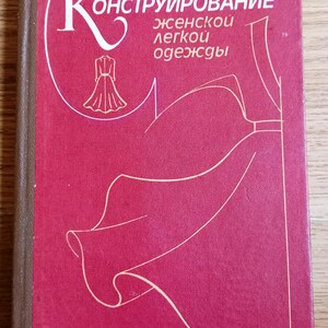 Puede incluir: Un libro de tapa dura rojo con lomo marrón que presenta texto cirílico blanco que dice "Конструирование женской легкой одежды" e "И. М. Братчик". La portada muestra un dibujo lineal blanco de un vestido y patrones de prendas abstractos.