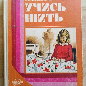 Op de afbeelding: Een hardcover boek met een oranje kaft met de Russische tekst R. I. EGOROVA V. P. MONASTYRNAYA en UCHIS SHIT. De illustratie op de kaft toont een persoon die een bloemrijke stof naait naast een paspop en een naaimachine.