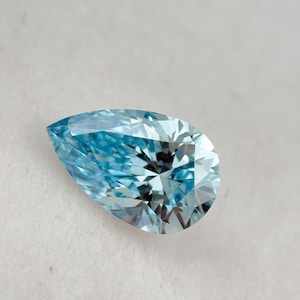 Puede incluir: Una gema azul claro en forma de pera con múltiples facetas. La gema se encuentra sobre un fondo blanco, mostrando su claridad y brillo. El corte de la piedra crea un juego de luces y sombras.