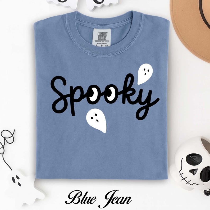 K&ouml;nnte beinhalten: Ein blaues Jeans-T-Shirt mit dem Wort "Spooky" in schwarzer Schrift und wei&szlig;en Geistergrafiken. Das Shirt hat einen Rundhalsausschnitt und kurze &Auml;rmel. Der Text "Blue Jean" ist unten auf dem Shirt aufgedruckt.