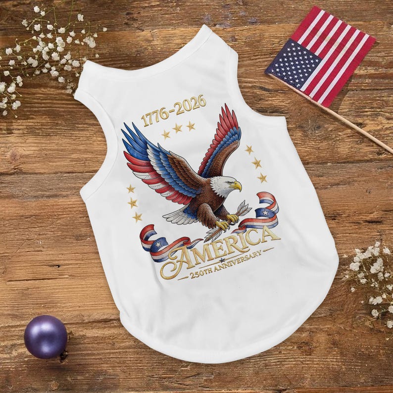 May include: White dog tank top with a patriotic design featuring a bald eagle with red, white, and blue wings, holding a sprig. The text reads "AMERICA 250th Anniversary" and "1776-2026". An American flag is also present.