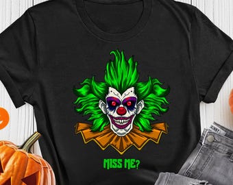 May include: Black t-shirt featuring a scary clown face with green hair, a red nose, and the text "MISS ME?". The shirt is paired with gray jeans, a carved pumpkin, and a small pumpkin decoration, perfect for Halloween.