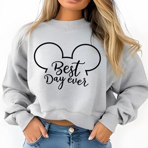 May include: A light gray sweatshirt with a black Mickey Mouse ear design and the text "Best Day ever". The sweatshirt is a crew neck style.