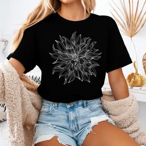 May include: Black t-shirt with a large white floral design. The detailed flower graphic is the focal point, with intricate lines defining the petals. The shirt is worn with denim shorts. The overall style is casual.
