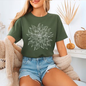 May include: An olive green t-shirt with a white floral design. The short-sleeved top is paired with denim shorts. The image suggests a casual, comfortable style, ideal for everyday wear. The shirt is made of a soft material.