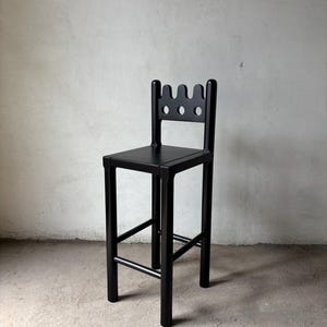 Pu&ograve; includere: Uno sgabello da bar nero con un design unico dello schienale con tre intagli ad arco. Lo sgabello ha una seduta quadrata e un poggiapiedi. Le gambe sono dritte e robuste e il design generale &egrave; minimalista e moderno.