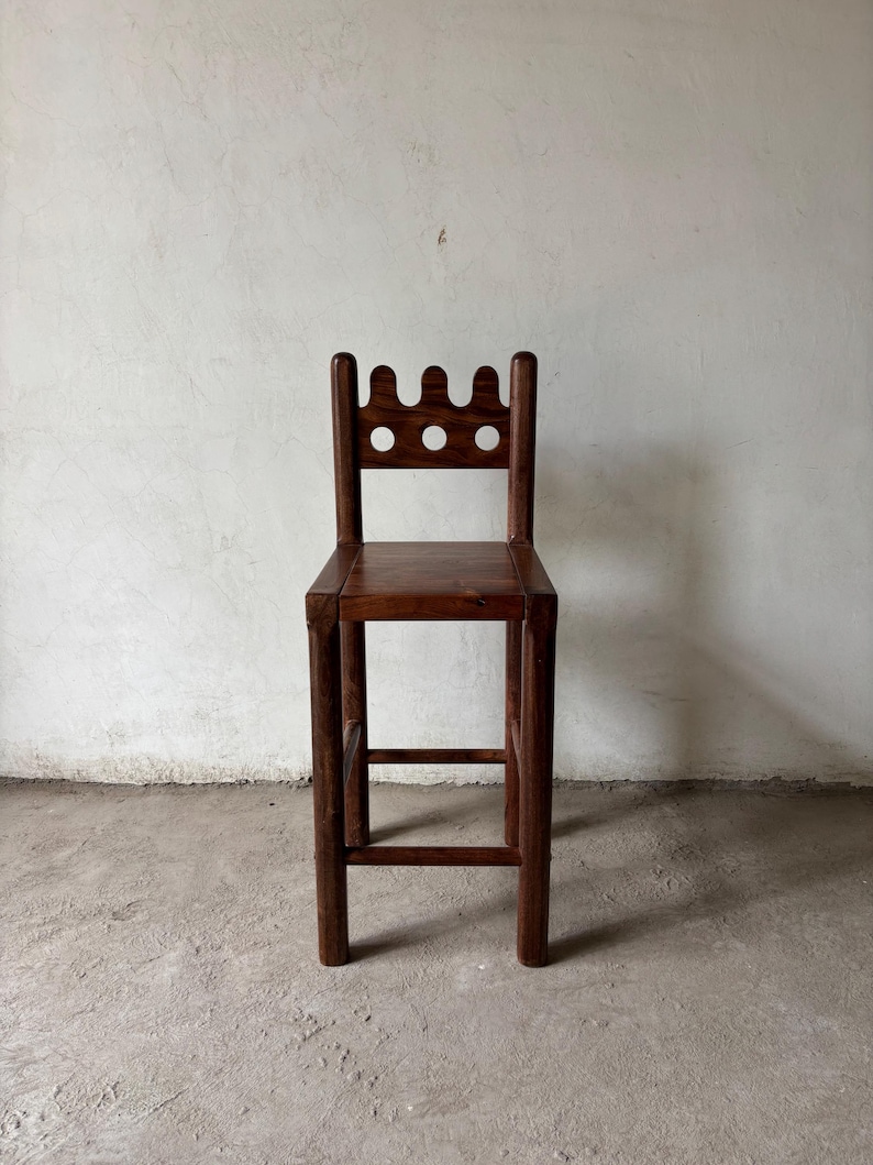Pu&ograve; includere: Sgabello da bar in legno marrone scuro con schienale decorativo con tre intagli circolari. Lo sgabello ha una seduta quadrata e gambe robuste, che mostrano un design semplice e rustico. Lo sgabello &egrave; realizzato in legno massello.