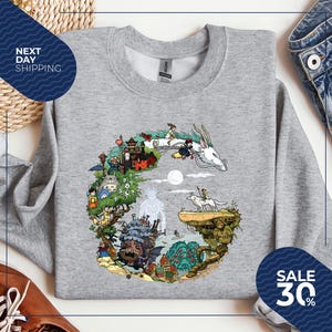 a gray sweatshirt with a colorful illustration of a fantastical scene, including a castle, a dragon, and various other characters and elements. The sweatshirt is displayed on a white background, and there are two blue sale signs in the image, indicating a sale or discount.
