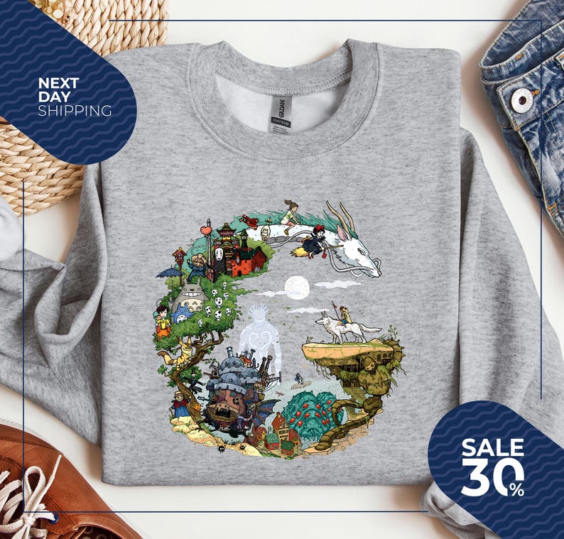 a gray sweatshirt with a colorful illustration of a fantastical scene, including a castle, a dragon, and various other characters and elements. The sweatshirt is displayed on a white background, and there are two blue sale signs in the image, indicating a sale or discount.