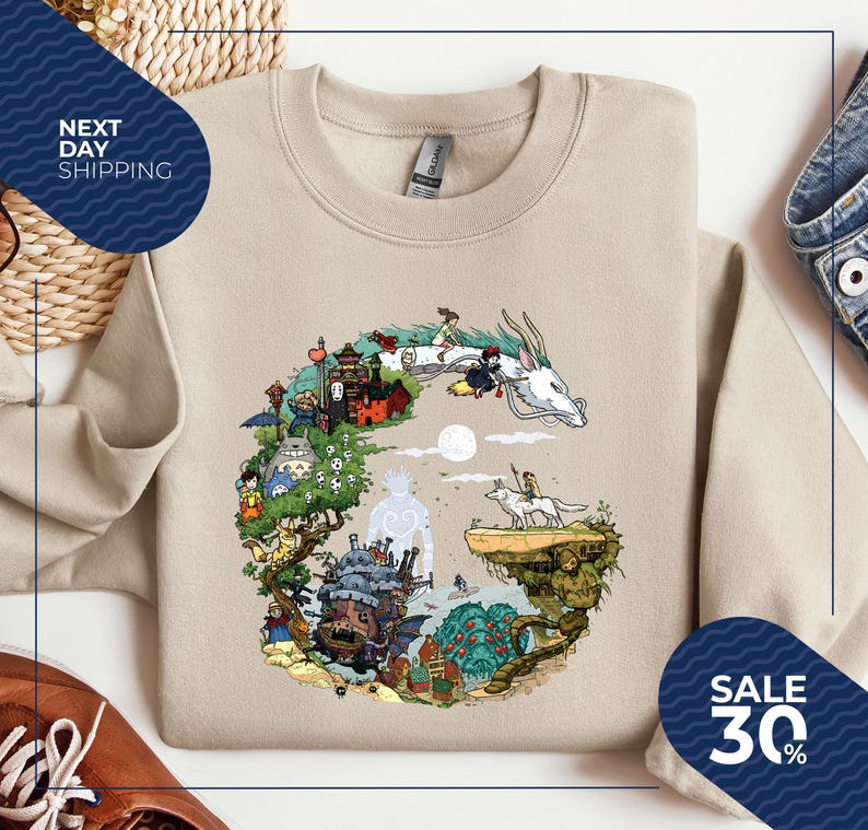 a beige sweatshirt with a colorful illustration of a dragon and various fantastical elements, such as a castle, trees, and people, all set against a whimsical landscape. The sweatshirt is displayed on a white background, and there are other clothing items and accessories visible in the image.