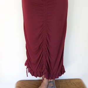May include: A long burgundy skirt with a gathered detail at the waist and a ruffled hem.