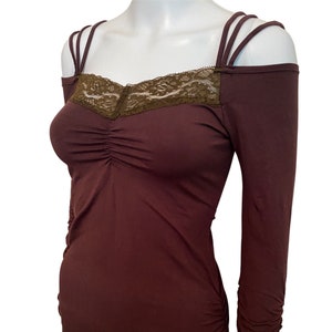 May include: A brown long-sleeved top with a lace neckline and a gathered bodice. The top has thin straps that cross over the shoulders.