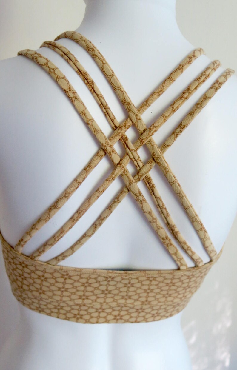May include: A beige sports bra with a criss-cross back design. The straps are made of a patterned fabric with a geometric design.