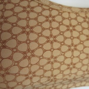 May include: A beige fabric with a brown geometric pattern. The pattern is made up of small, rounded shapes that are arranged in a repeating pattern.