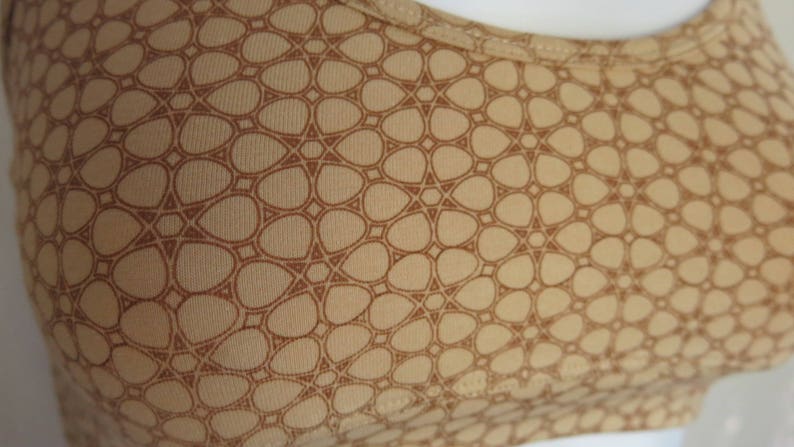 May include: A beige fabric with a brown geometric pattern. The pattern is made up of small, rounded shapes that are arranged in a repeating pattern.