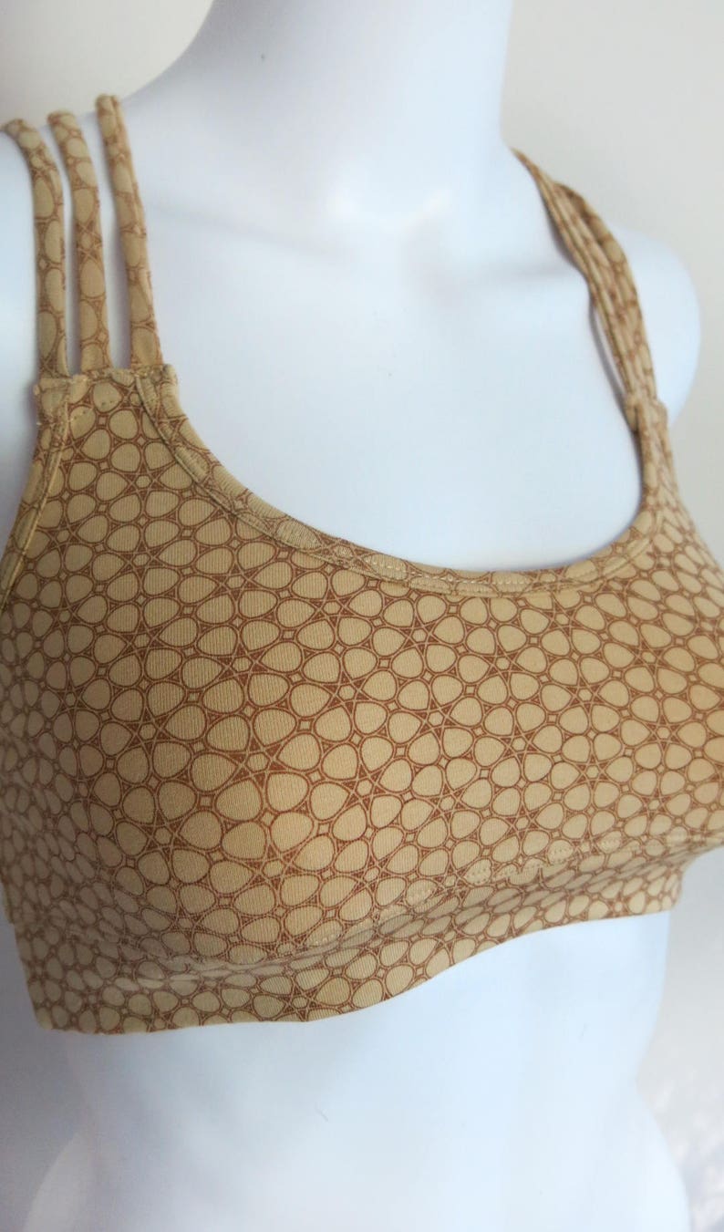 May include: A brown and tan sports bra with a geometric pattern. The bra has a scoop neck and adjustable straps.