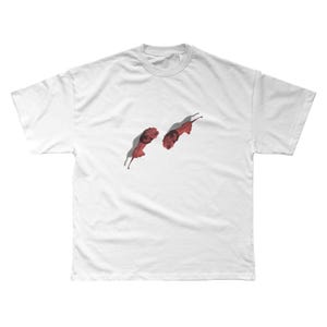 May include: White t-shirt featuring two red lion illustrations. The lions are depicted in a stylized, artistic manner, with detailed manes and bodies. The design is centered on the shirt, creating a bold visual statement.