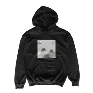 May include: Black hooded sweatshirt with a front pocket and drawstring hood. The sweatshirt features a square graphic on the chest with a grayscale landscape image and two circular symbols. A casual, comfortable garment.