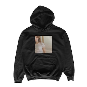 May include: Black hooded sweatshirt with a front pocket and a drawstring hood. The sweatshirt features a rectangular image on the front, depicting a person in a white t-shirt. The image on the sweatshirt has a vintage aesthetic.