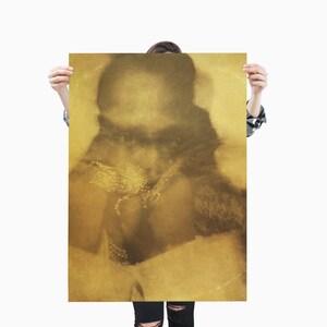 May include: A sepia-toned print featuring a blurred image of a person with a dark silhouette. The person is holding the print, which has a golden hue. The print's design includes a floral element and a fur-like texture.