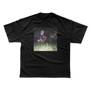 May include: Black t-shirt with a graphic image of two people in a natural setting. The image has a blurred, artistic quality. The shirt has a crew neck and short sleeves. The image also includes a parental advisory label.