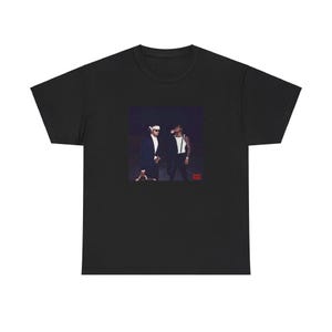 May include: Black t-shirt featuring a graphic of two men in suits and sunglasses. The image is a photograph with a dark background. The t-shirt is made of a soft, comfortable material.