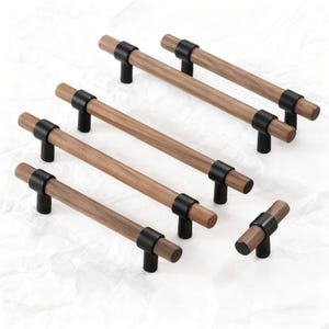 May include: A selection of wooden cabinet pulls with a dark finish. The pulls feature a cylindrical wooden handle and are accented with black metal hardware. The hardware connects the handle to the cabinet. The pulls are arranged on a white surface.