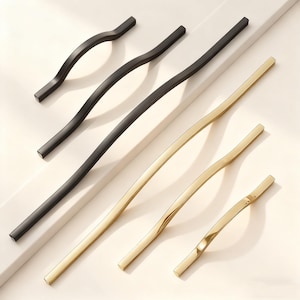 May include: A selection of contemporary cabinet handles in black and gold finishes. The handles have a curved, minimalist design and are displayed on a white surface. The lengths vary, with the longest being approximately 30 cm.