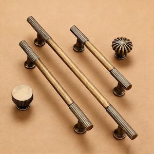 May include: A set of antique brass cabinet handles and knobs. The set includes two long bar pulls, a round knob, and a decorative knob. The pulls have a ribbed design on the ends. The hardware is designed for cabinets and drawers.