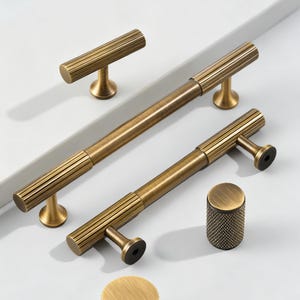 May include: A collection of antique brass cabinet hardware, including bar pulls, a T-knob, and a cylindrical knob. The hardware features a ribbed design and a warm, aged finish, suitable for kitchen or bathroom cabinetry.