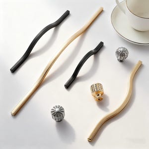 May include: An assortment of cabinet hardware, including black and gold wavy handles, and decorative knobs. The knobs are silver and gold, with crystal-like embellishments. The handles are in varying lengths.