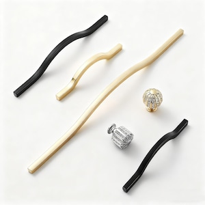 Könnte beinhalten: Eine Auswahl an Schrankbeschlägen, darunter schwarze und goldfarbene Griffe und dekorative Knöpfe. Die Griffe haben geschwungene und gerade Designs. Ein Knopf ist goldfarben mit einem kristallartigen Design, ein anderer silberfarben mit einem geometrischen Muster.