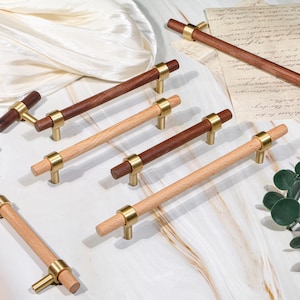 Puede incluir: Un conjunto de tiradores de madera para armarios con detalles de latón. Los tiradores presentan tonos de madera variados, incluyendo marrón claro y oscuro, y están dispuestos sobre una superficie de mármol. Para muebles y decoración del hogar, medidas en centímetros.