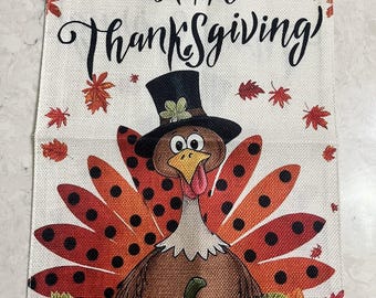 May include: Thanksgiving-themed decorative banner featuring a cartoon turkey wearing a top hat, with a pumpkin and floral accents. The banner reads "Happy Thanksgiving" in black script, surrounded by autumn leaves.