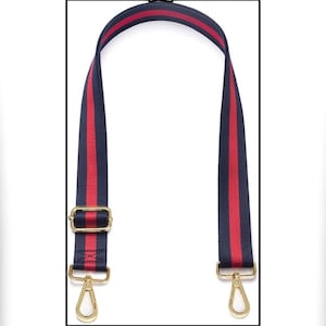 Puede incluir: Una correa de bolso a rayas azul marino y rojo con herrajes met&aacute;licos dorados. La correa presenta una franja roja central flanqueada por rayas azul marino. Se ven cierres y una hebilla de metal dorado.