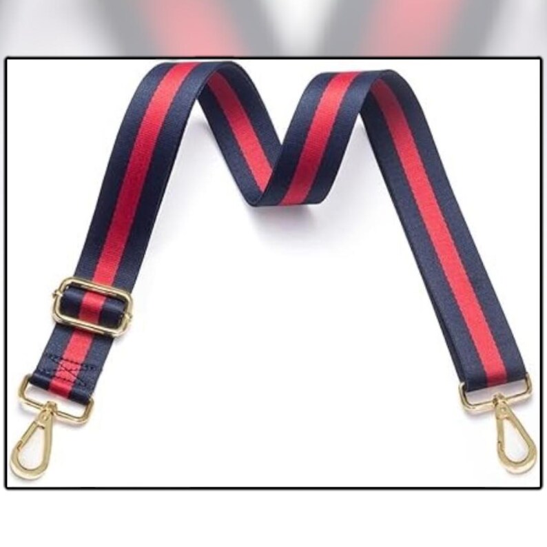 Puede incluir: Una correa de bolso a rayas azul marino y rojo con herrajes met&aacute;licos dorados. La correa tiene un patr&oacute;n repetido de una raya roja entre dos rayas azul marino. Los cierres met&aacute;licos dorados est&aacute;n en cada extremo.