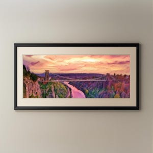 Puede incluir: Pintura enmarcada de un puente colgante sobre un río al atardecer. El cielo es una mezcla de rosas y naranjas, con el puente y los árboles en tonos morados y verdes. La obra de arte está en un marco negro.
