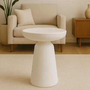 May include: A white, modern side table with a round top and a conical base. The table is made of a solid material and stands on a light-colored rug. The background includes a beige armchair, a wooden cabinet, and a potted plant.