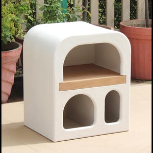 Puede incluir: Horno de exterior blanco con parte superior arqueada, estante de madera y dos aberturas arqueadas. El horno est&aacute; hecho de un material texturizado. El horno es de color neutro y encajar&iacute;a en cualquier espacio exterior. Dimensiones: aprox. 60 cm x 60 cm x 90 cm.