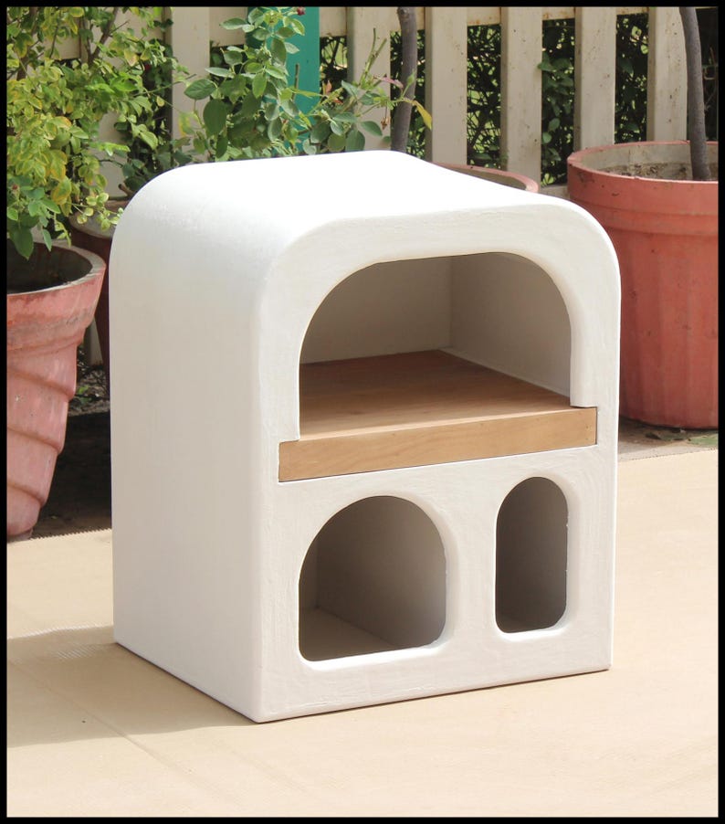 Puede incluir: Horno de exterior blanco con parte superior arqueada, estante de madera y dos aberturas arqueadas. El horno est&aacute; hecho de un material texturizado. El horno es de color neutro y encajar&iacute;a en cualquier espacio exterior. Dimensiones: aprox. 60 cm x 60 cm x 90 cm.