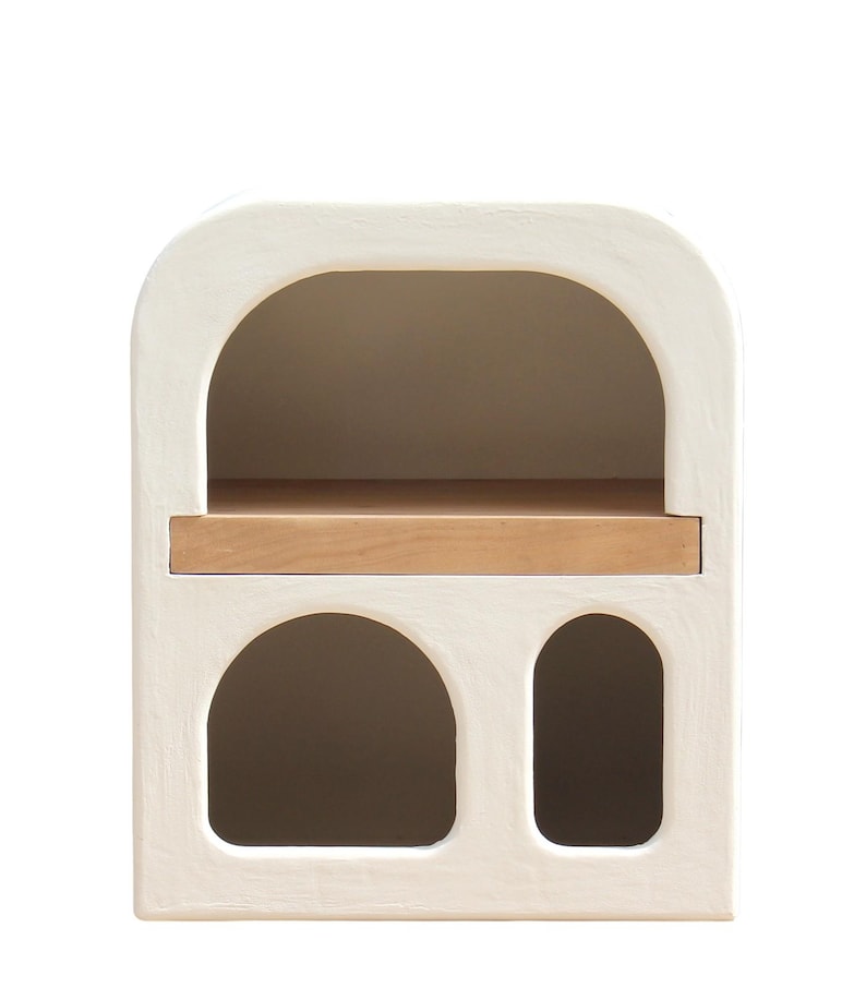 Puede incluir: Una mesita de noche blanca con parte superior arqueada, estante de madera y dos aberturas arqueadas. La mesita tiene un acabado texturizado y un dise&ntilde;o minimalista. Dimensiones: aproximadamente 61 cm de alto, 46 cm de ancho y 30 cm de profundidad, ideal para dormitorio.