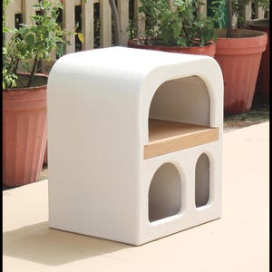 Puede incluir: Una mesa auxiliar blanca con una parte superior arqueada, un estante de madera y dos recortes arqueados. La mesa est&aacute; hecha de un material texturizado y mide aproximadamente 61 cm de alto, 46 cm de ancho y 30 cm de profundidad. El dise&ntilde;o es moderno y minimalista.