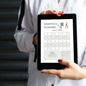 Könnte beinhalten: Ein schwarzes Tablet mit einem Monatsplaner für Juli. Der Planer enthält Abschnitte für Daten, Notizen und Checklisten. Das Tablet wird von einer Person in einem weißen Hemd gehalten. Der Text "MONTHLY PLANNER" steht oben.