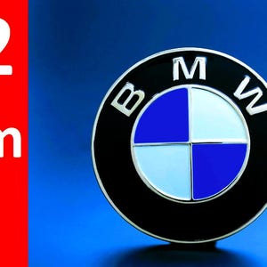 May include: A BMW emblem with a black border, silver accents, and a blue and white center. The emblem is set against a blue background. The number "82 mm" is displayed in white text on a red background.