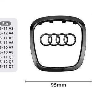 Może przedstawiać: Czarny emblemat samochodowy z logo Audi, składający się z czterech zazębiających się pierścieni. Emblemat ma 9,5 cm szerokości i 9,7 cm wysokości. Lista po lewej stronie wskazuje kompatybilność z różnymi modelami Audi, w tym A3, A4, A5, A6, A7, A8, Q3, Q5 i Q7.