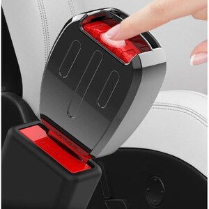 K&ouml;nnte beinhalten: Nahaufnahme einer schwarzen und verchromten Autosicherheitsgurtschnalle mit rotem Entriegelungsknopf. Ein Finger dr&uuml;ckt den Knopf. Der Sitz ist aus wei&szlig;em Leder.