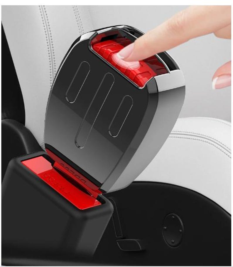 K&ouml;nnte beinhalten: Nahaufnahme einer schwarzen und verchromten Autosicherheitsgurtschnalle mit rotem Entriegelungsknopf. Ein Finger dr&uuml;ckt den Knopf. Der Sitz ist aus wei&szlig;em Leder.