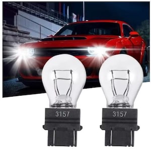 Puede incluir: Dos bombillas automotrices transparentes 3157 con bases negras en primer plano. Un coche deportivo rojo con faros brillantes en el fondo. Las bombillas est&aacute;n dise&ntilde;adas para uso automotriz.