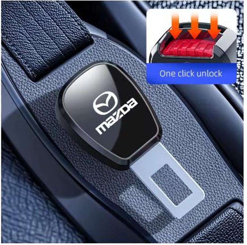 May include: Black car seat belt buckle with the Mazda logo in white. The buckle is in a car interior setting. The image also shows a close-up of the seat belt release button with the text "One click unlock".